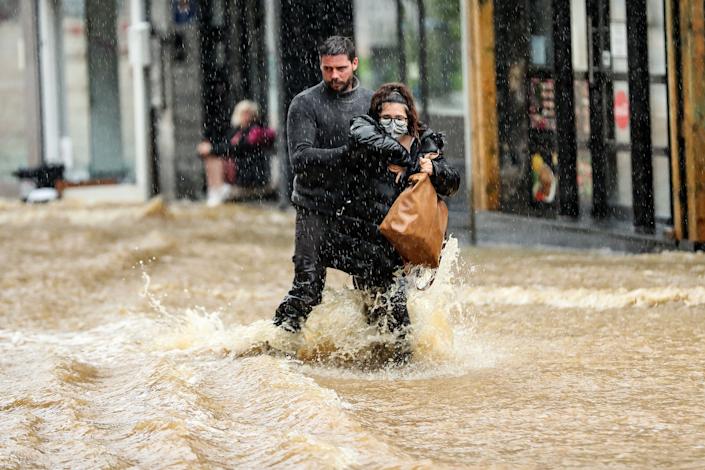 Un bărbat ajută o femeie să navigheze joi pe o stradă inundată din centrul orașului Spa, Belgia