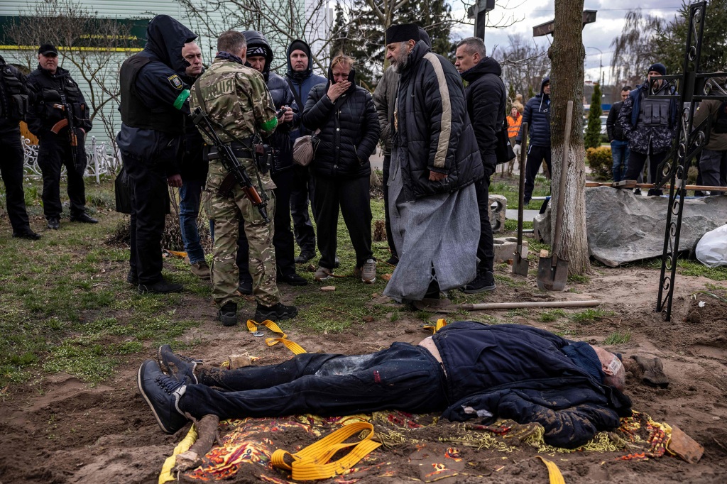 Un preot și rudele lui interacționează cu cadavrul primarului Gostomel, Yuri Prilypko, care este înmormântat lângă o biserică din satul Gostomel, regiunea Kiev, pe 12 aprilie 2022.