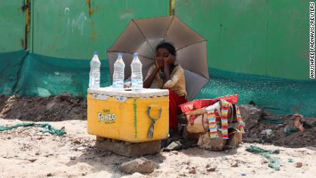 O fată care vinde apă folosește o umbrelă pentru a se proteja de razele soarelui în New Delhi.