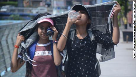 Fetele își acoperă capul în timp ce merg și beau apă în căldura arzătoare a după-amiezii din Mumbai.